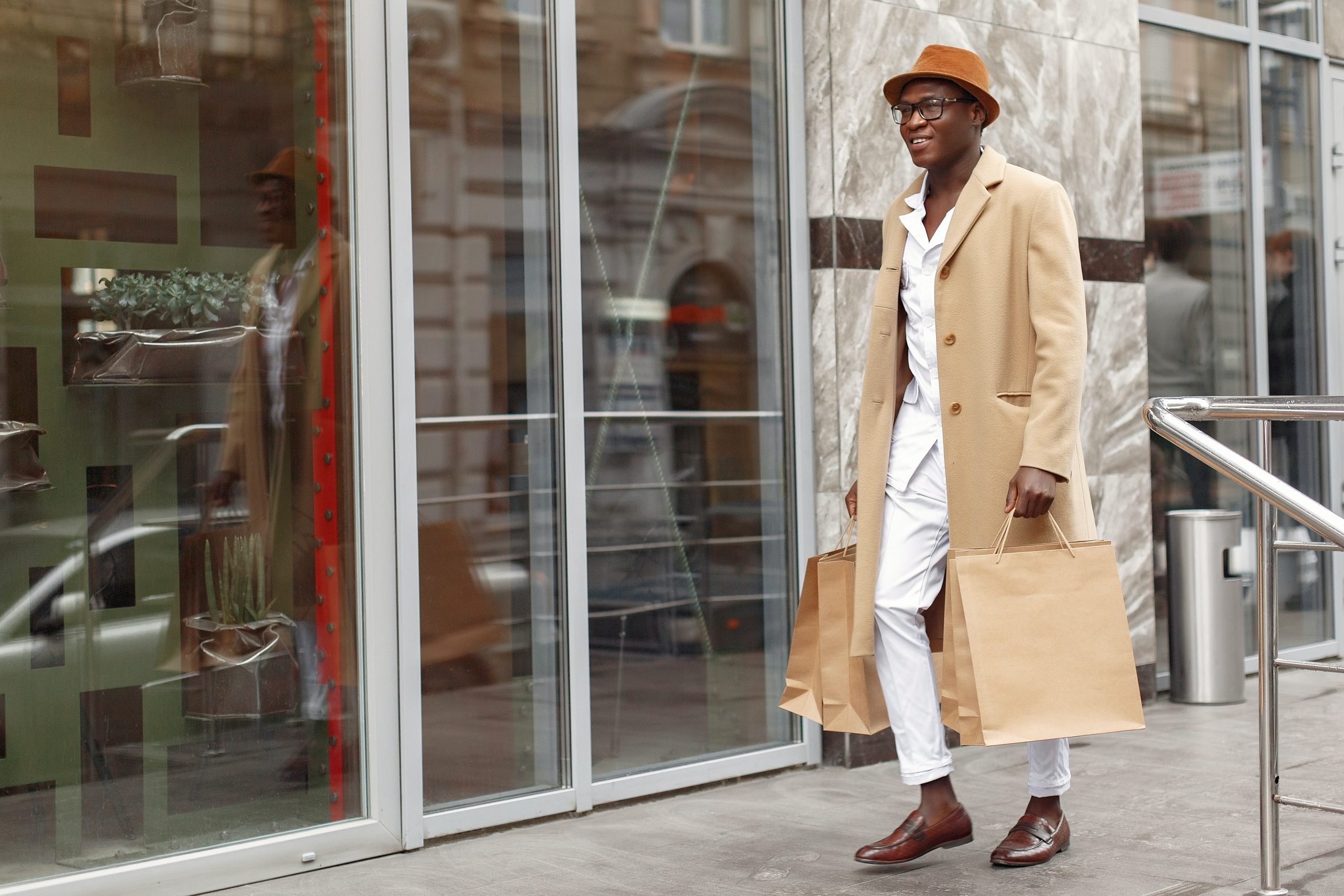 Man walking in beige pea coat with two shopping bags