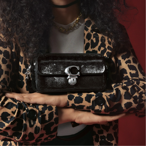 A person wearing a Cheetah print blazer and holding a black sequin purse