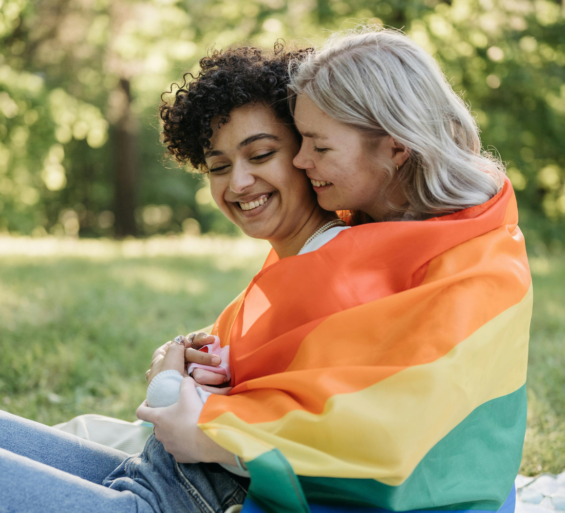 Two women sitting in the grass with a flag wrapped around them